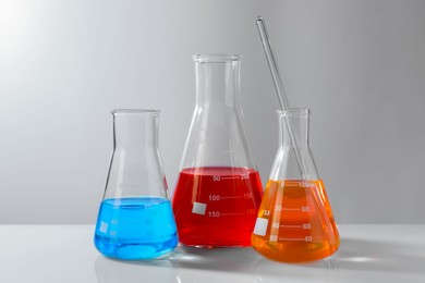 Photo of Glass flasks with colorful liquids on white table against grey background