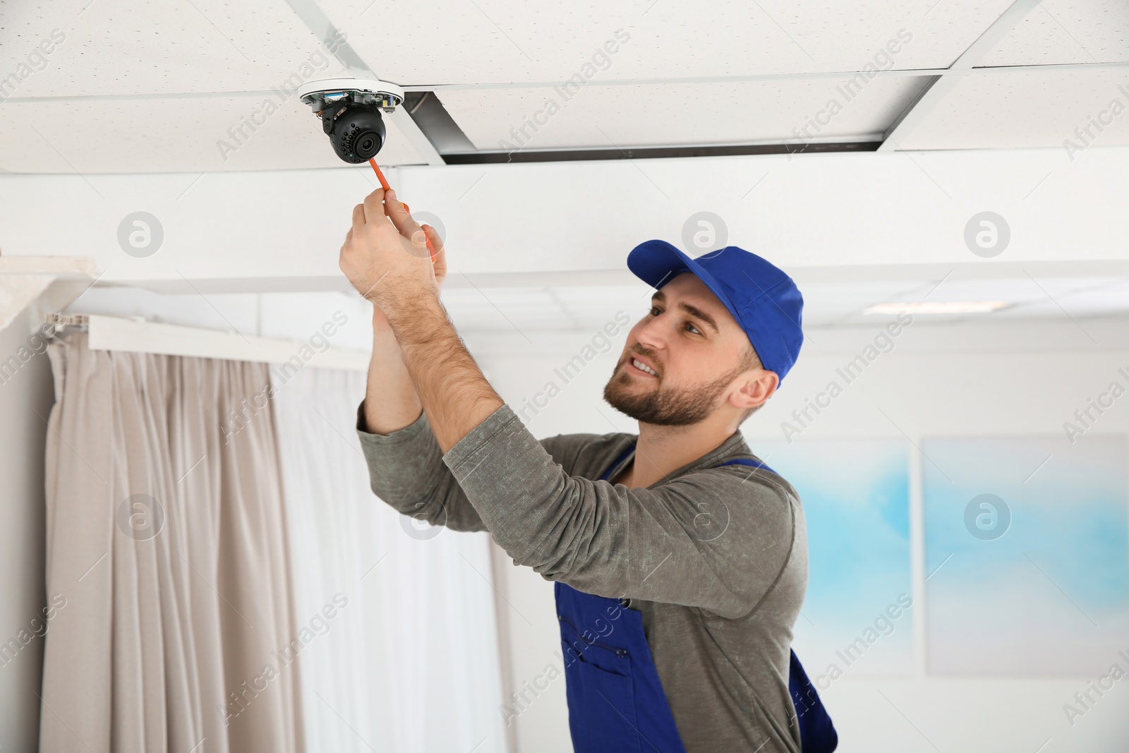 Photo of Electrician with screwdriver repairing CCTV camera indoors