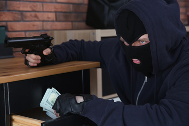 Dangerous masked criminal with gun stealing money from house