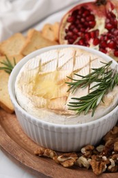 Photo of Board with tasty baked camembert and rosemary in bowl on table, closeup