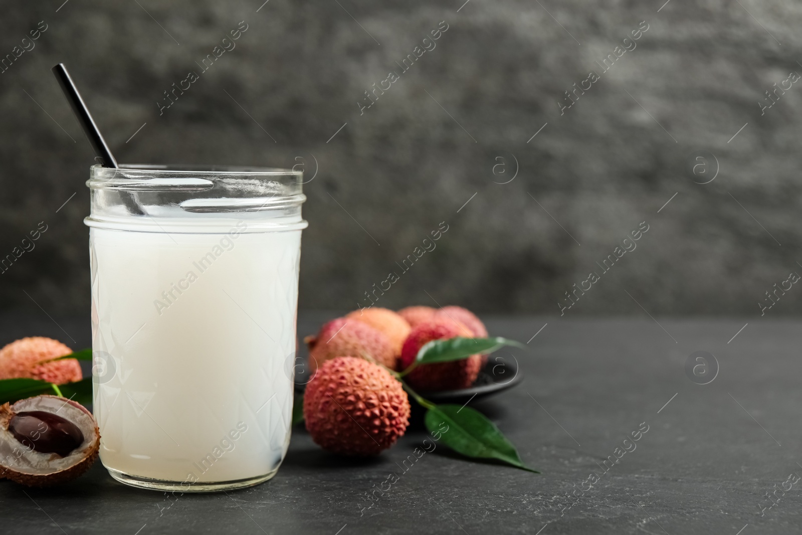 Photo of Fresh lychee juice and fruits on black table. Space for text