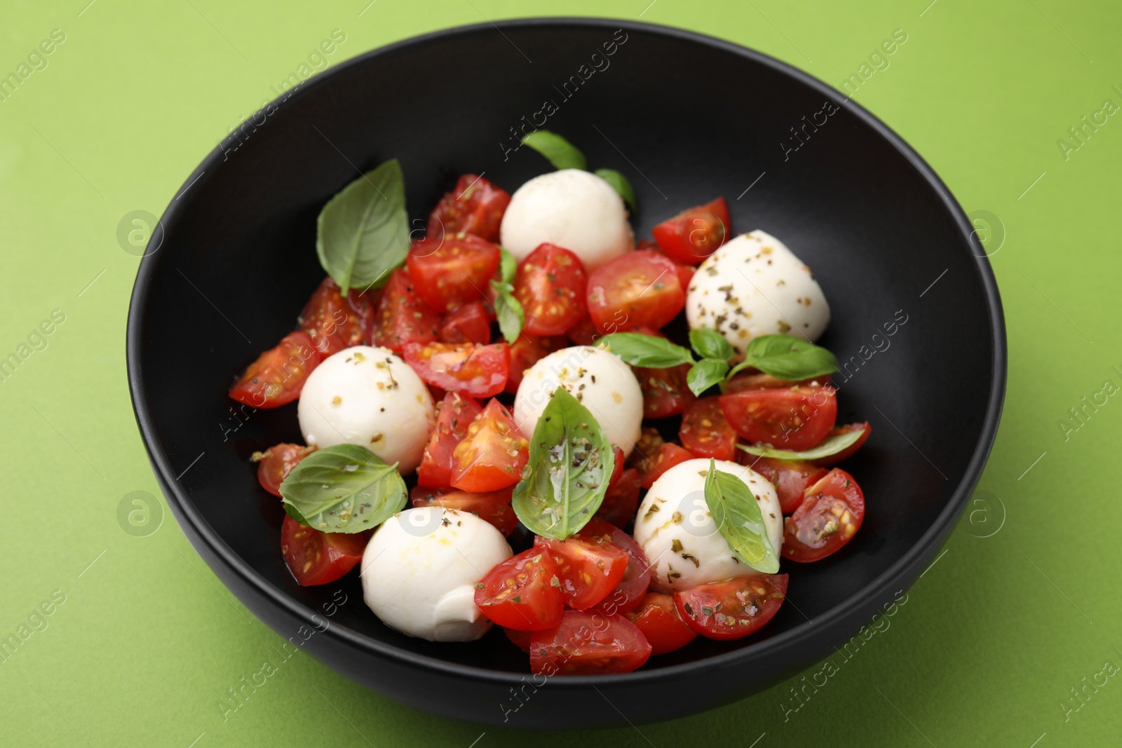 Photo of Tasty Caprese salad with tomatoes, mozzarella balls and basil on green background, closeup