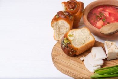 Photo of Delicious pampushky (buns with garlic), green onions and salo served for borsch on white wooden table, space for text. Traditional Ukrainian cuisine