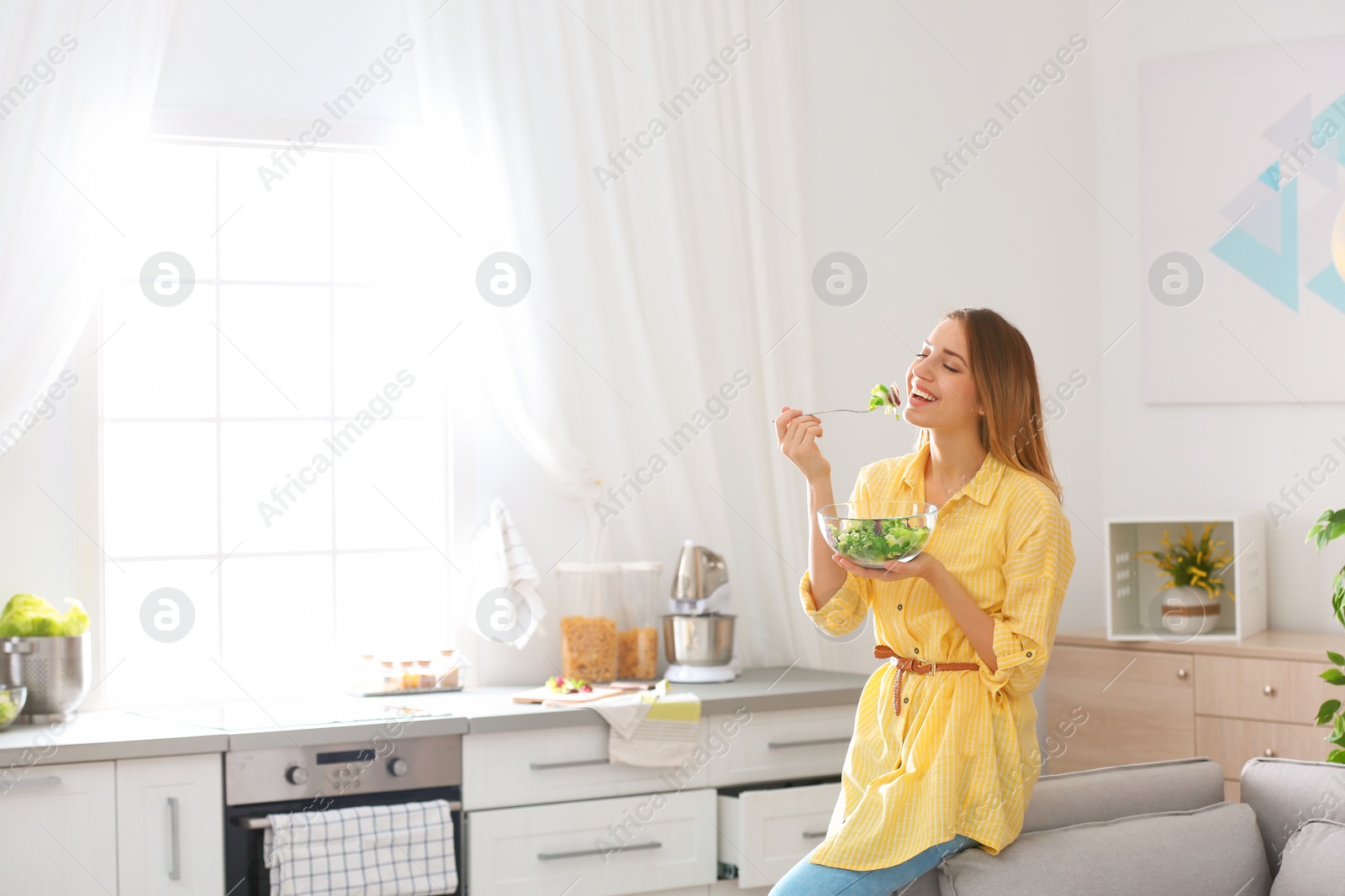 Photo of Happy young woman eating salad in kitchen, space for text. Healthy diet