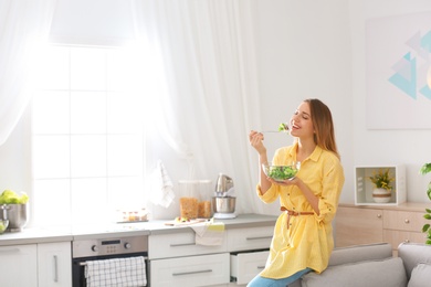 Happy young woman eating salad in kitchen, space for text. Healthy diet