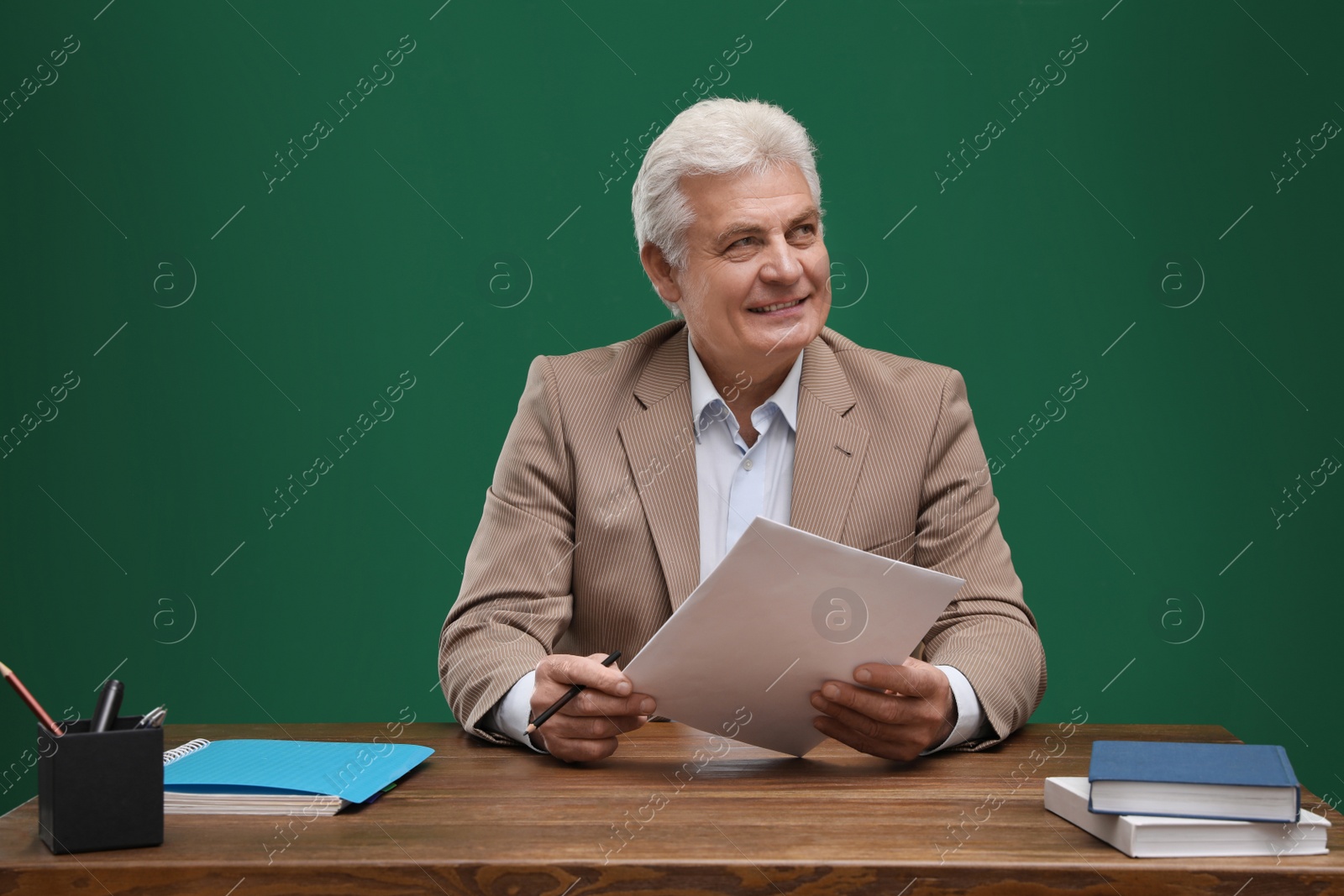 Photo of Portrait of senior teacher at table against green chalkboard