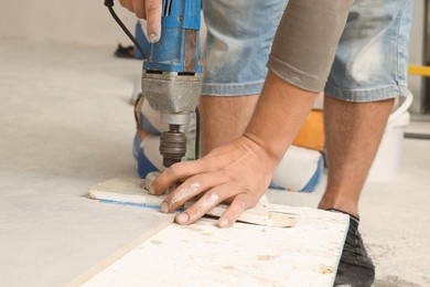 Worker with electric drill preparing tiles for installation indoors, closeup