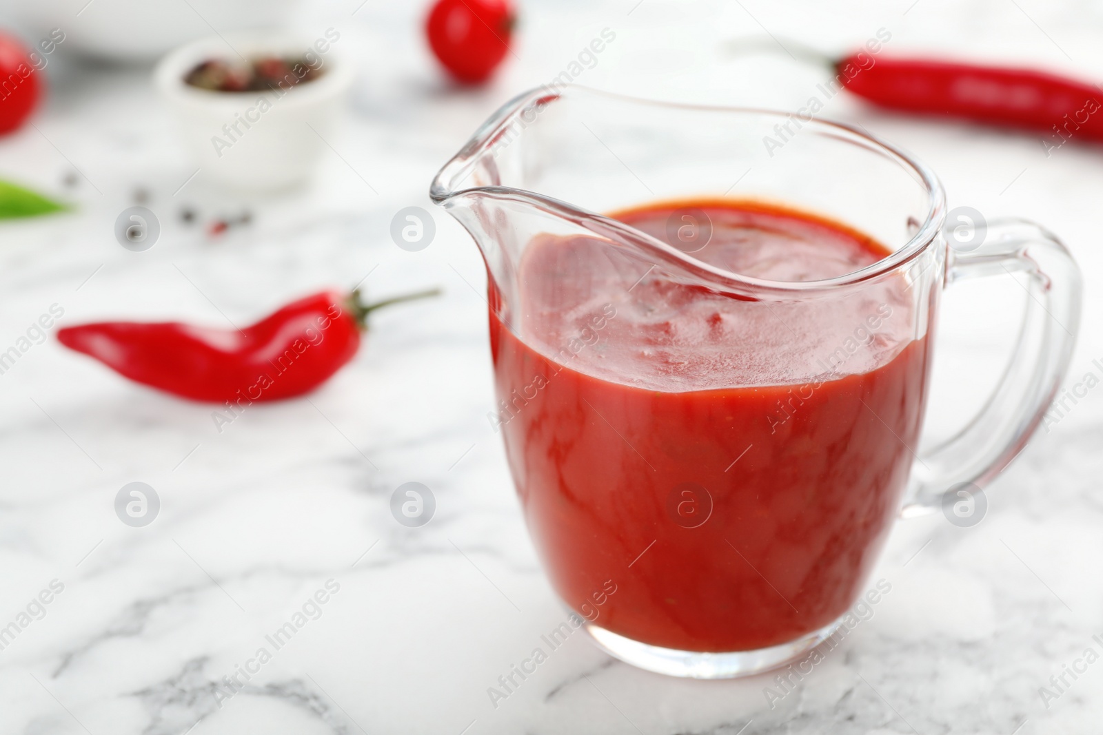 Photo of Jug with spicy chili sauce on marble table