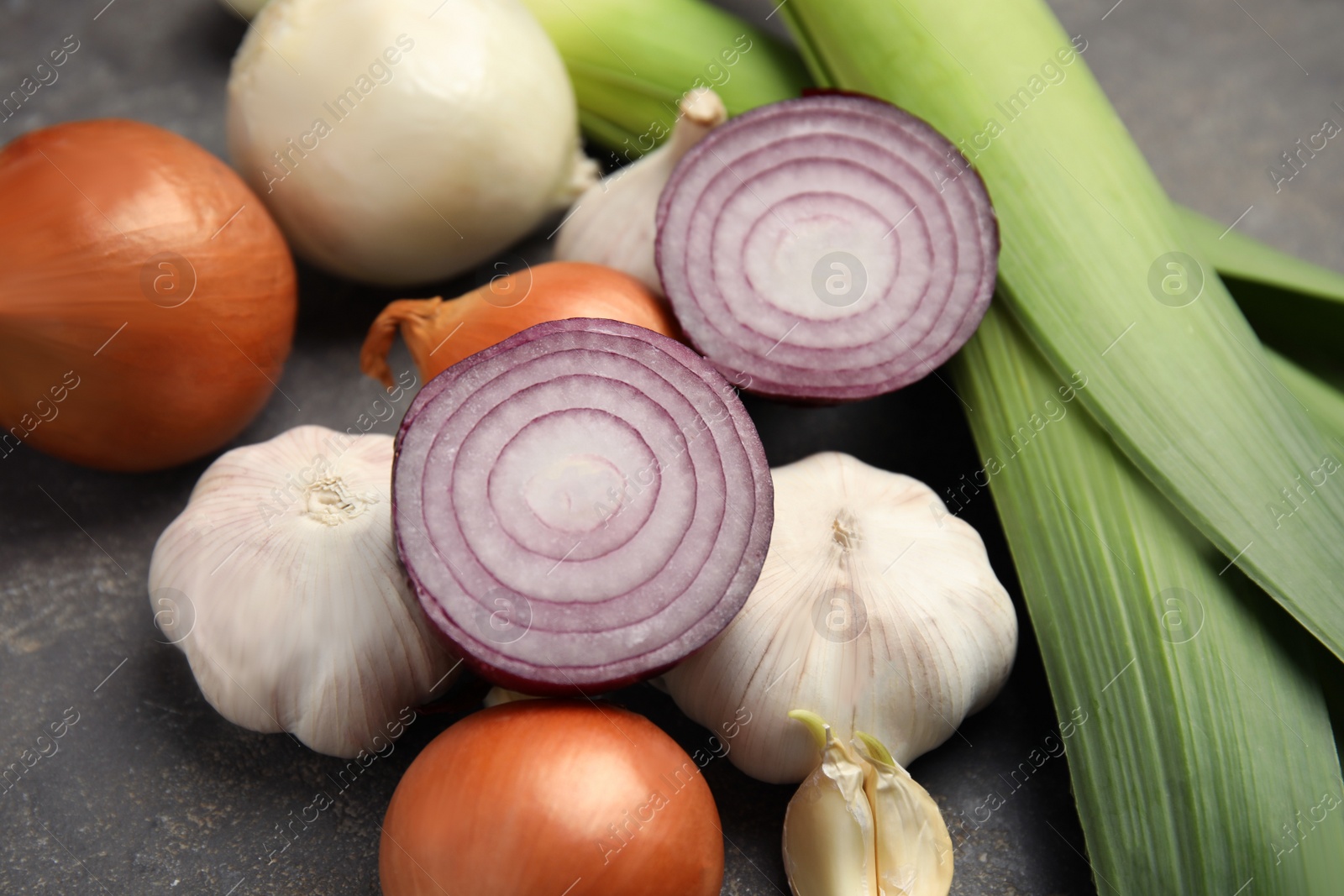 Photo of Fresh whole and cut onions, leeks, garlic on grey table, closeup
