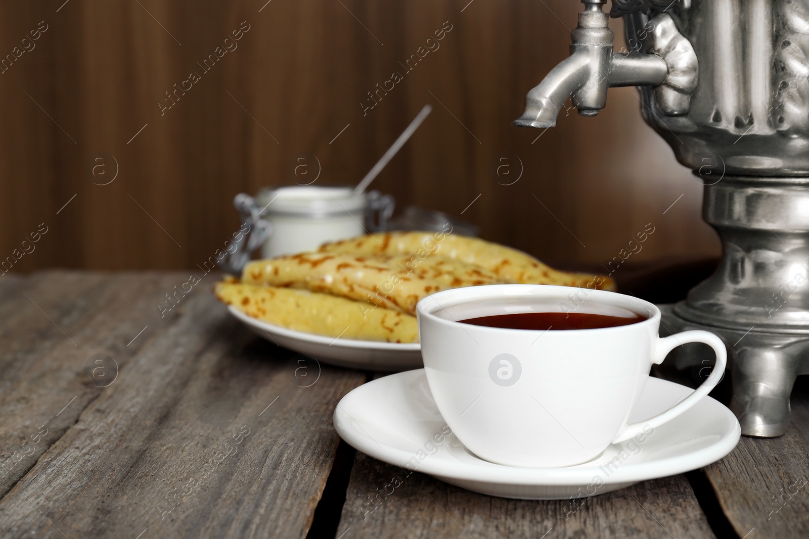 Photo of Vintage samovar, cup of hot drink and pancakes served on wooden table. Traditional Russian tea ceremony