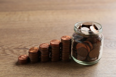 Photo of Glass jar and stacks of coins on wooden table. Money saving concept