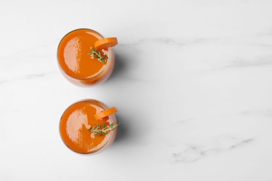 Glasses with healthy carrot juice on white marble table, flat lay. Space for text
