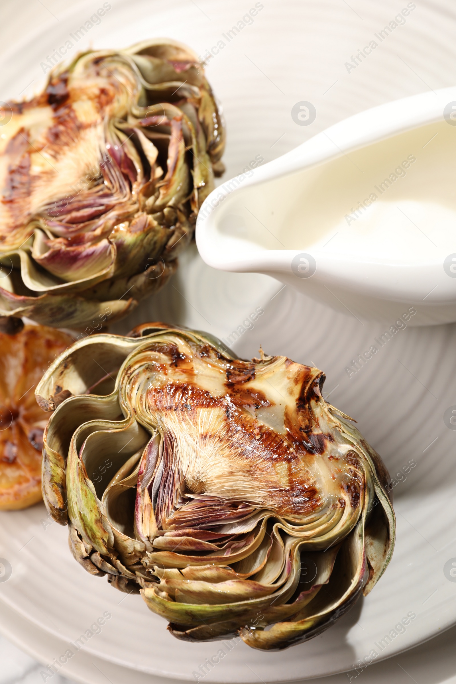 Photo of Tasty grilled artichokes and sauce on plate, closeup view