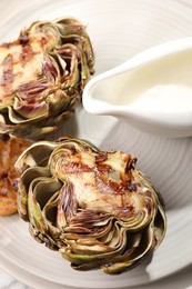 Tasty grilled artichokes and sauce on plate, closeup view