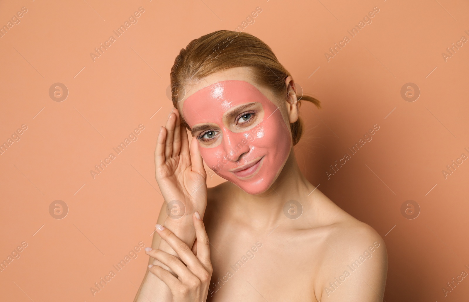 Photo of Young woman with pomegranate face mask on pale coral background