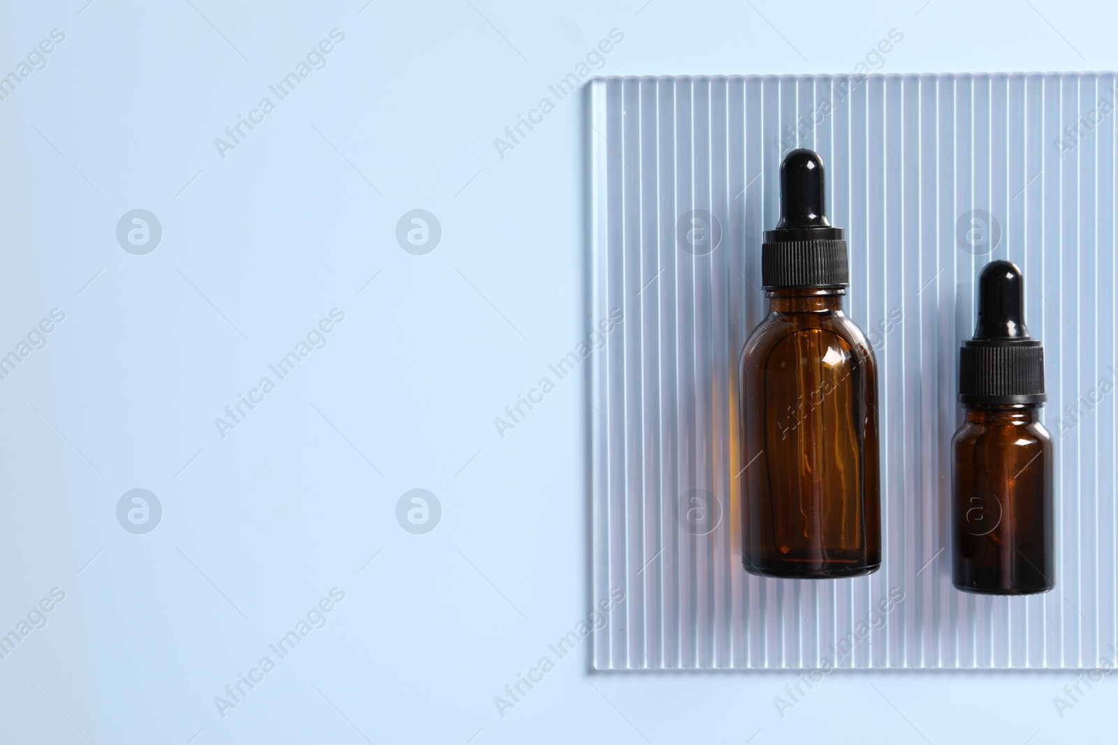 Photo of Bottles of cosmetic serum on light blue background, top view. Space for text