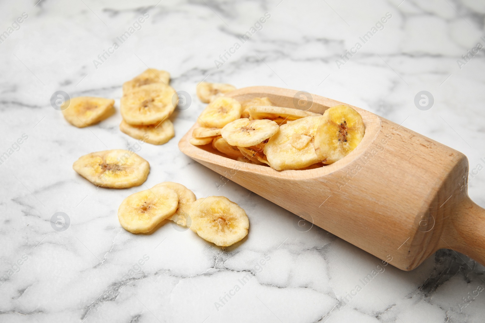 Photo of Scoop with banana slices on marble background, space for text. Dried fruit as healthy snack