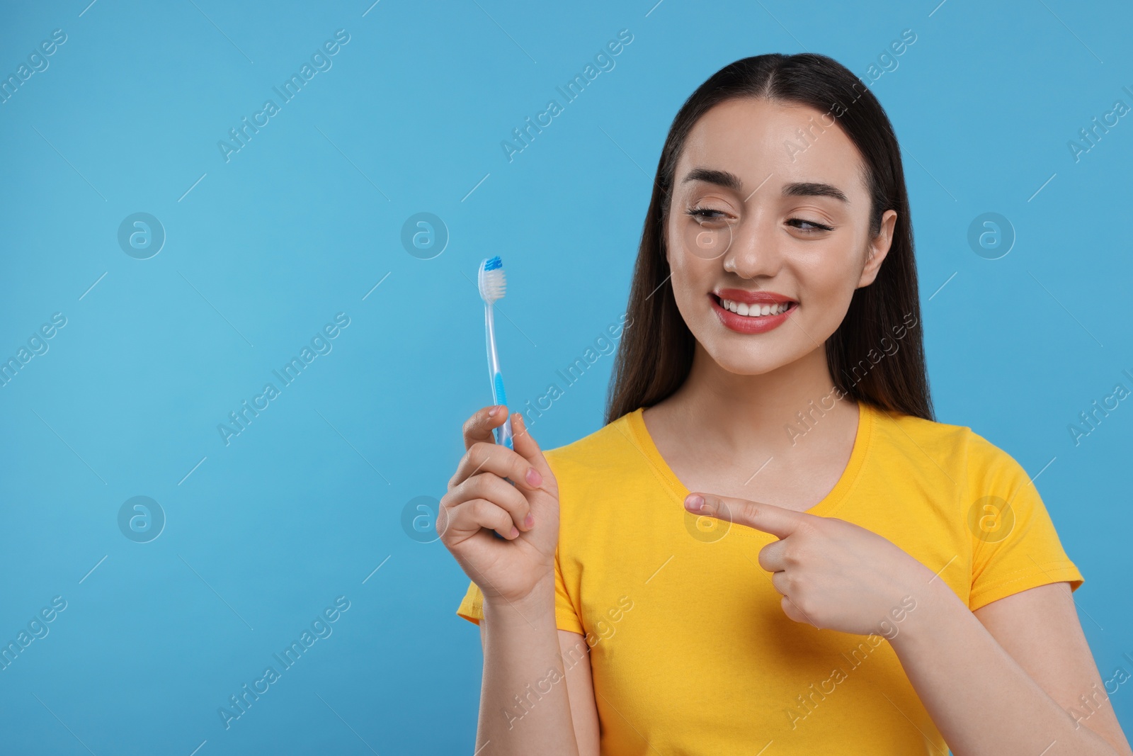 Photo of Happy young woman holding plastic toothbrush on light blue background, space for text