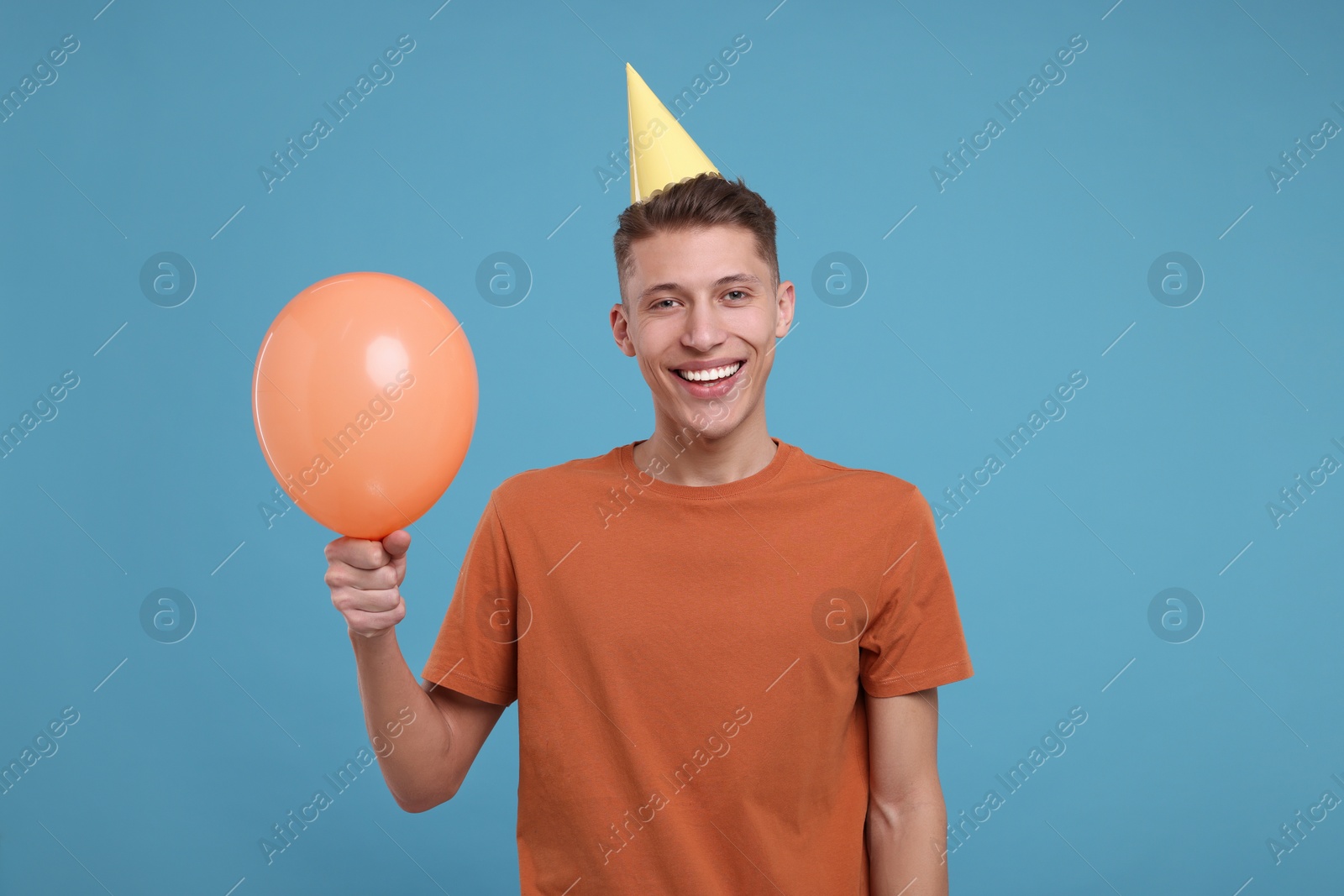 Photo of Happy man in party hat with balloon on light blue background