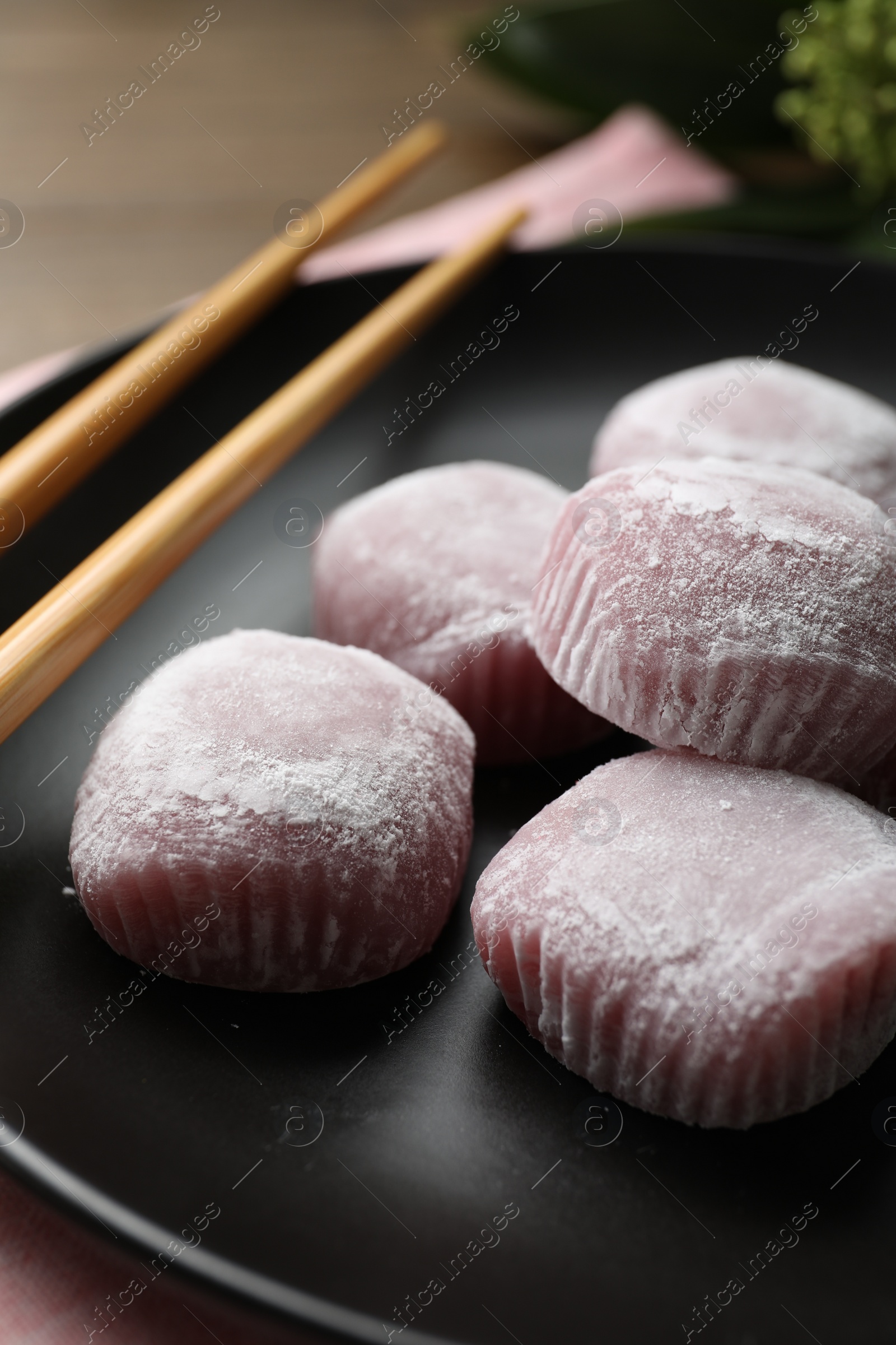 Photo of Delicious mochi and chopsticks on black plate, closeup. Traditional Japanese dessert