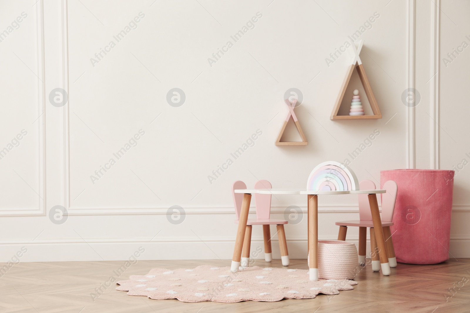 Photo of Cute child room interior with furniture, toys and wigwam shaped shelves on white wall. Space for text