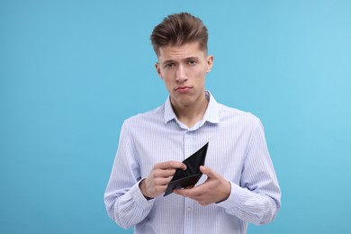 Photo of Upset man with empty wallet on light blue background