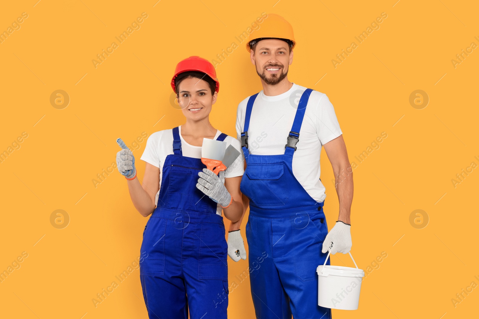 Photo of Professional workers with putty knives and plaster in hard hats on orange background