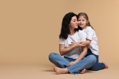 Beautiful mother with little daughter on beige background. Space for text