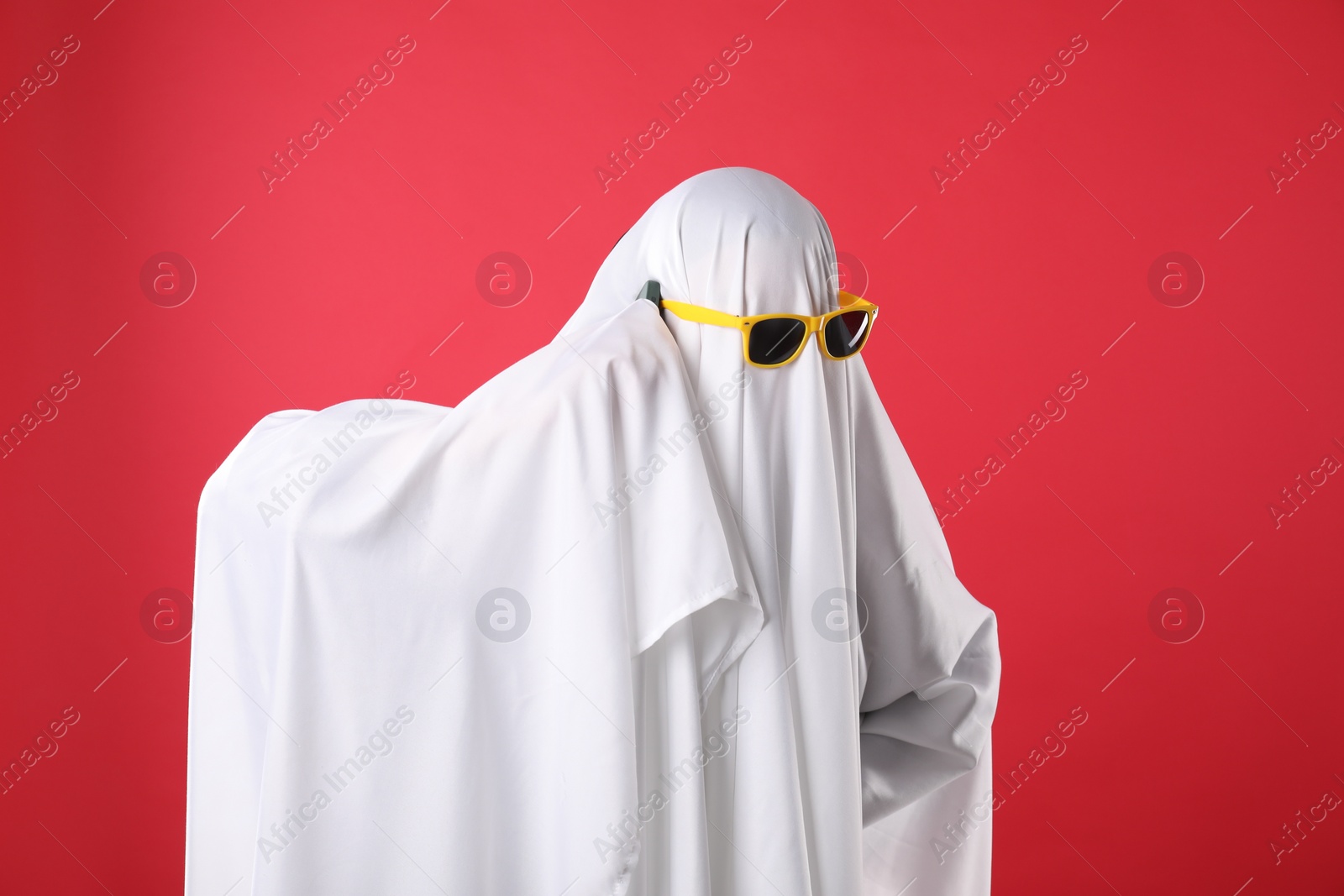 Photo of Person in ghost costume and sunglasses talking on smartphone against red background