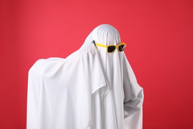 Person in ghost costume and sunglasses talking on smartphone against red background