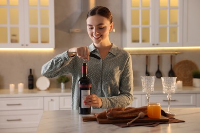 Photo of Romantic dinner. Woman opening wine bottle with corkscrew at table in kitchen
