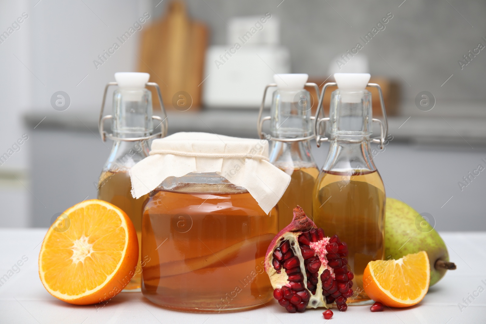 Photo of Homemade fermented kombucha and fresh fruits on white table in kitchen