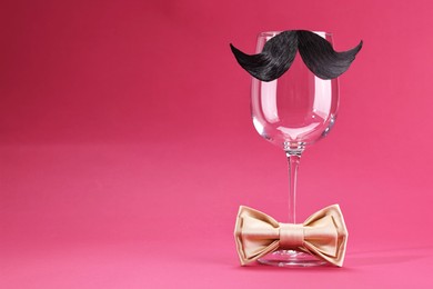 Man's face made of artificial mustache, bow tie and wine glass on crimson background. Space for text