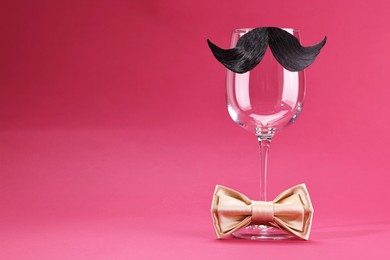 Photo of Man's face made of artificial mustache, bow tie and wine glass on crimson background. Space for text