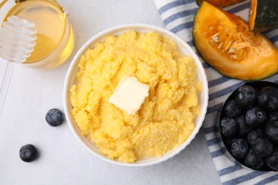 Photo of Tasty cornmeal with butter in bowl and products on light gray table, flat lay