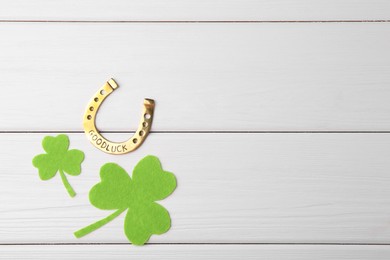 Photo of St. Patrick's day. Golden horseshoe and green decorative clover leaves on white wooden table, flat lay. Space for text