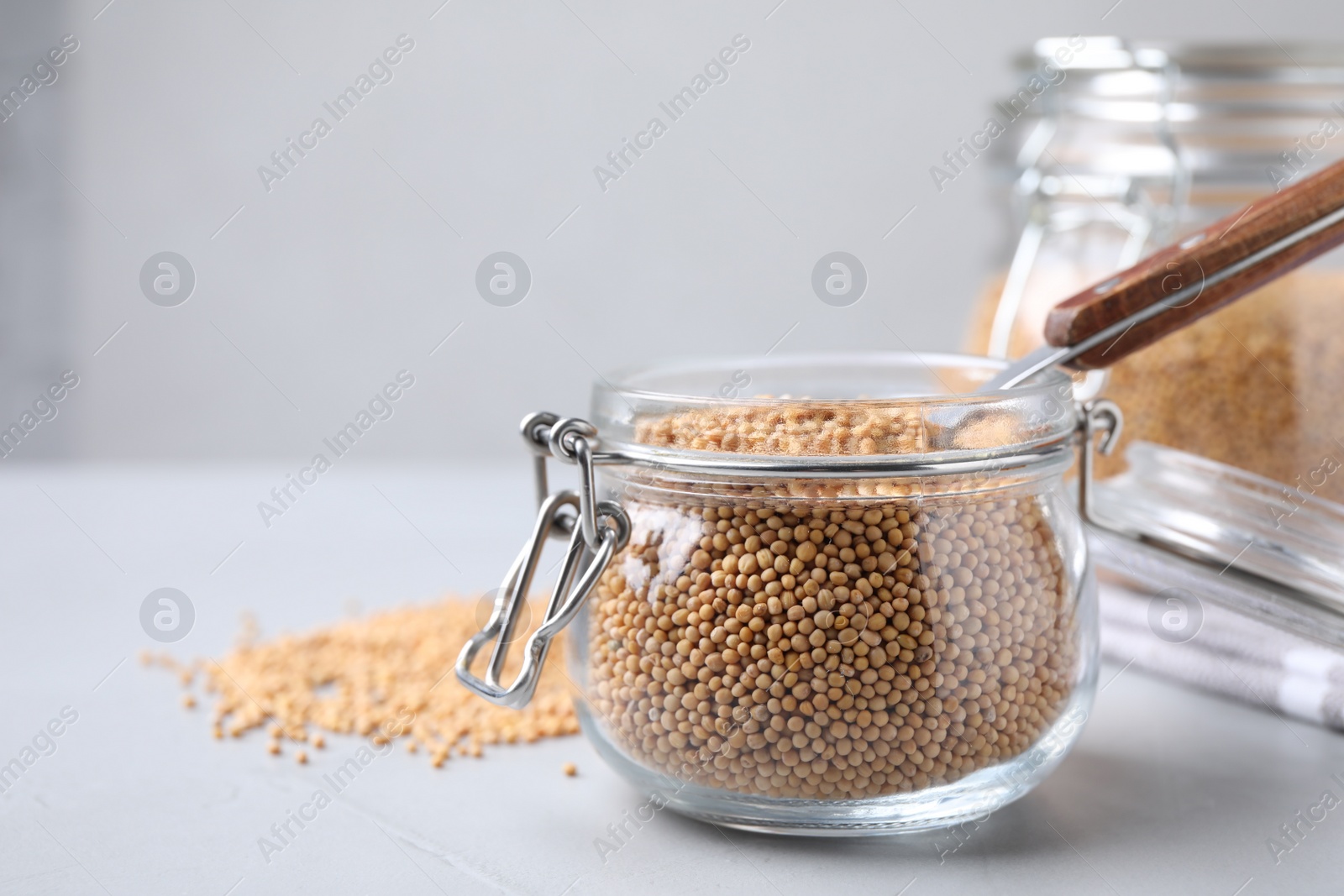 Photo of Mustard seeds with spoon in glass jar on light table. Space for text