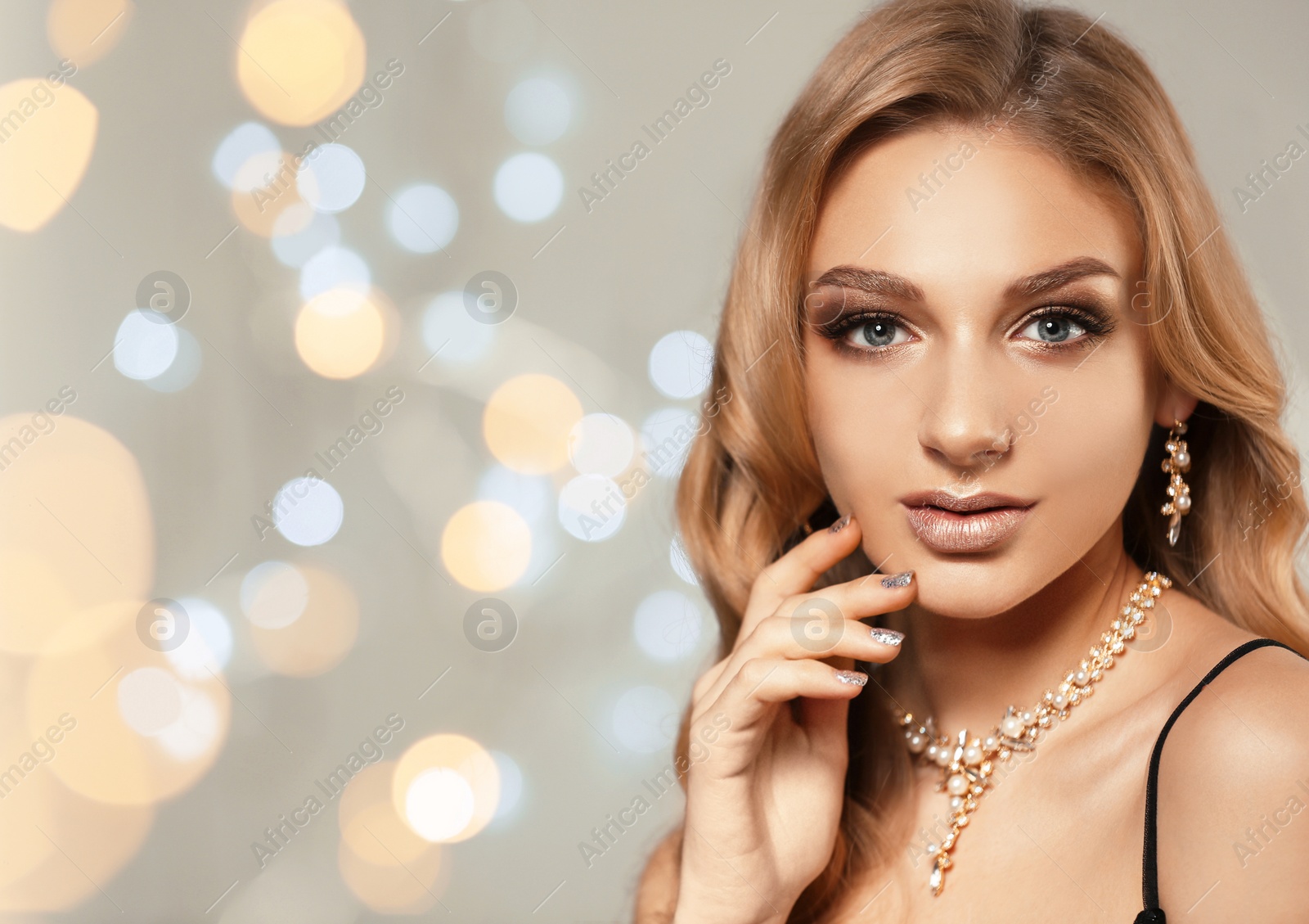 Photo of Beautiful young woman with elegant jewelry against defocused lights. Space for text