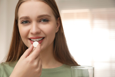 Young woman taking vitamin pill at home