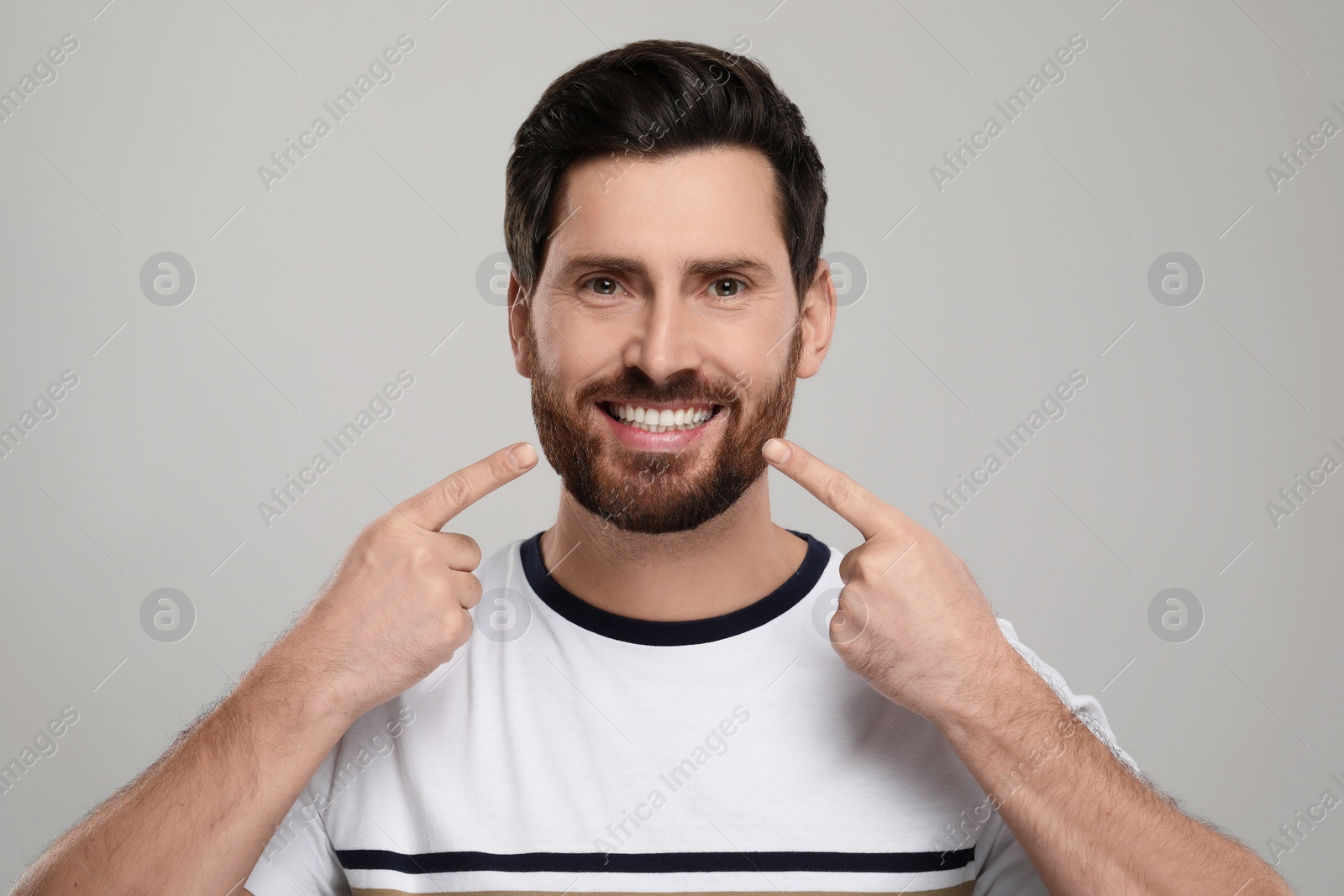 Photo of Smiling man pointing at his healthy clean teeth on light grey background