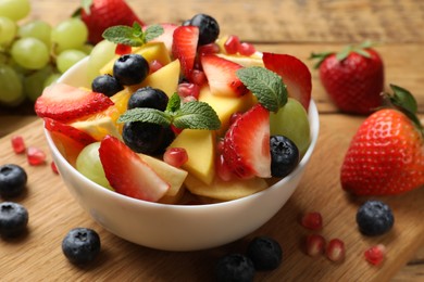 Tasty fruit salad in bowl and ingredients on wooden table, closeup