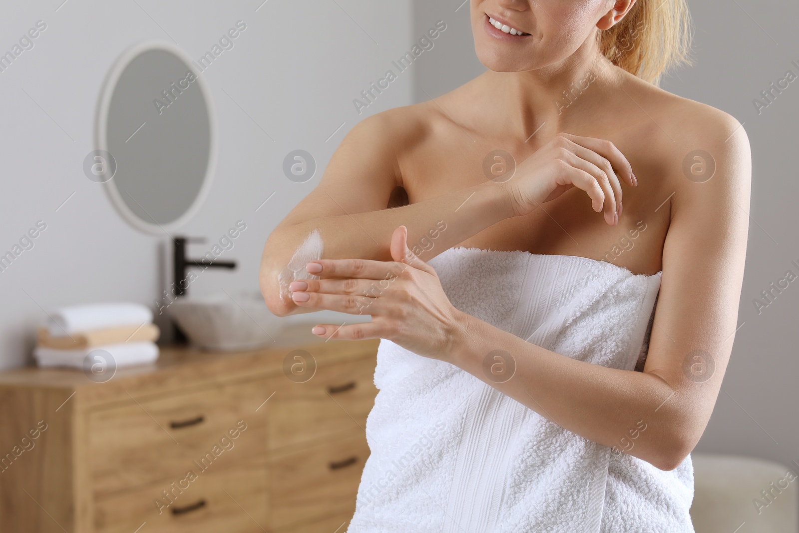 Photo of Woman applying body cream onto elbow in bathroom, closeup. Space for text