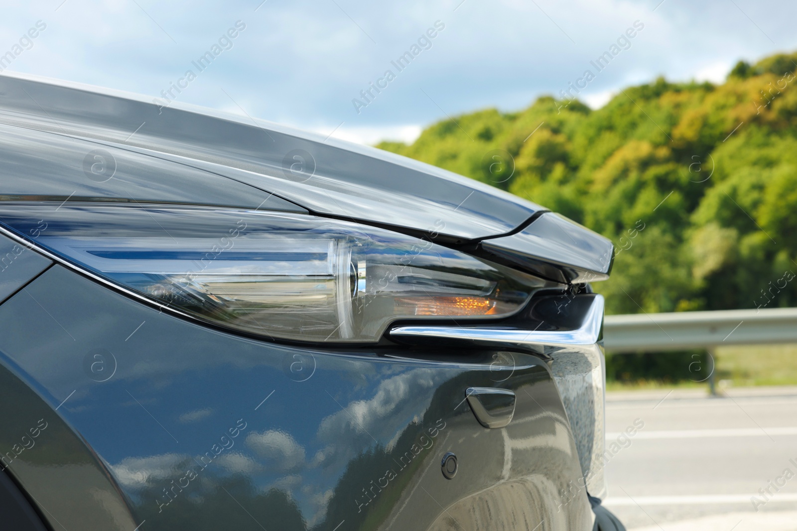 Photo of New black modern car on asphalt road, closeup of headlight