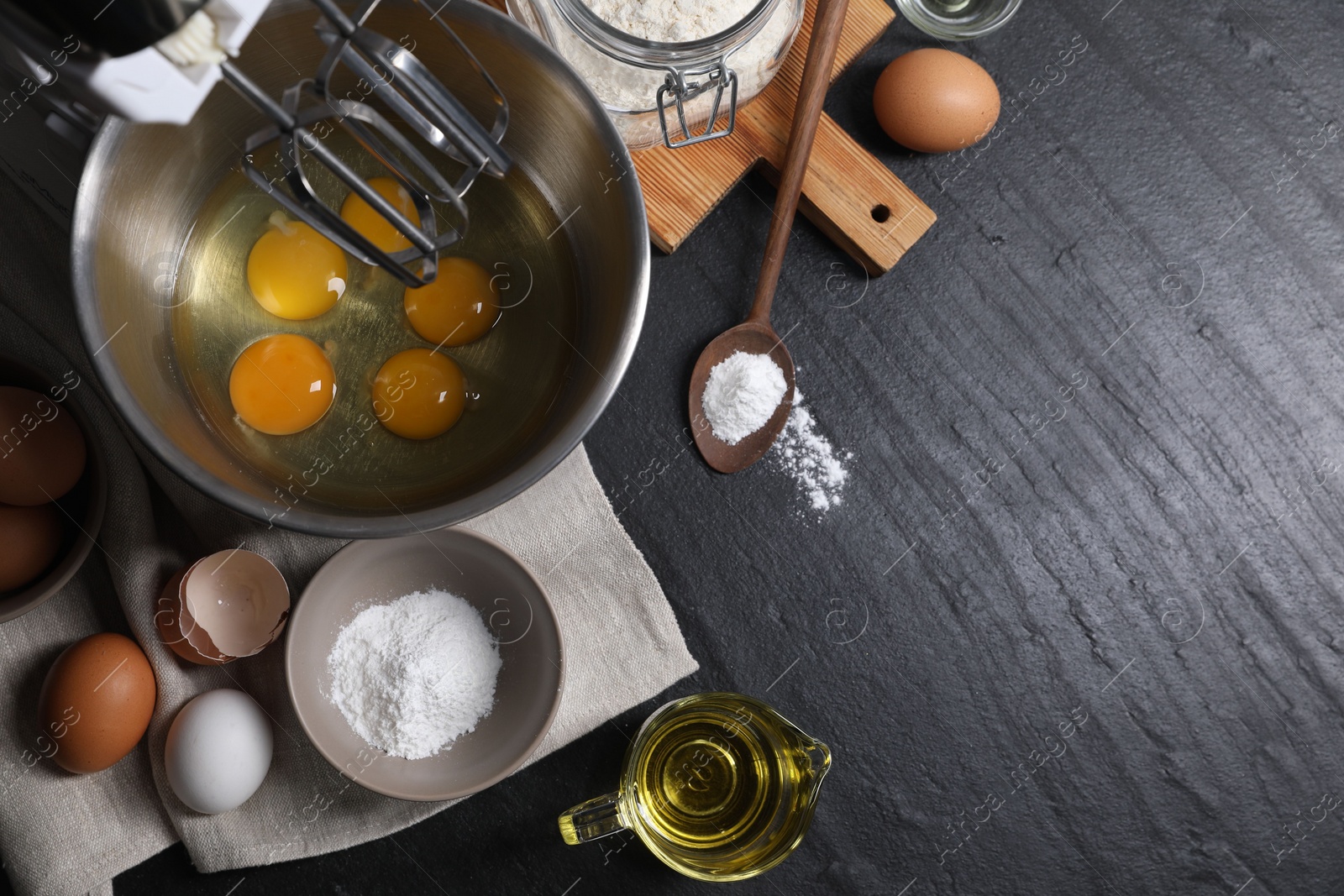 Photo of Making dough. Raw eggs in bowl of stand mixer and ingredients on black table, flat lay with space for text