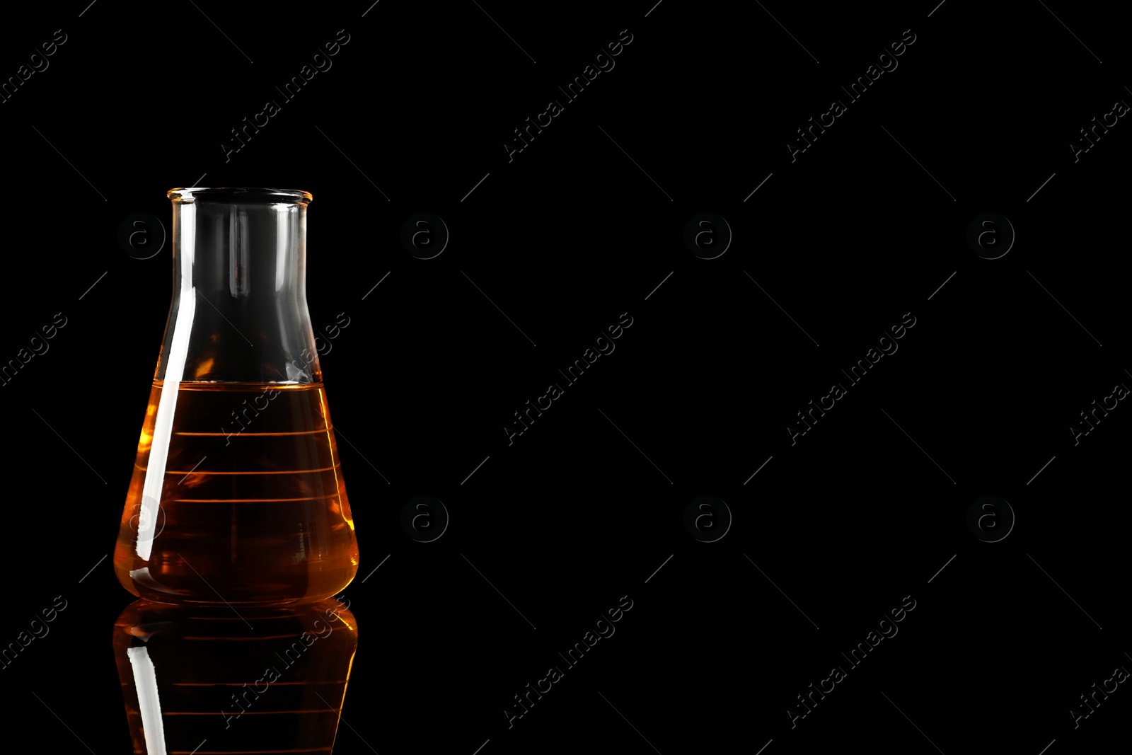 Photo of Glass flask with yellow oil on black background, space for text