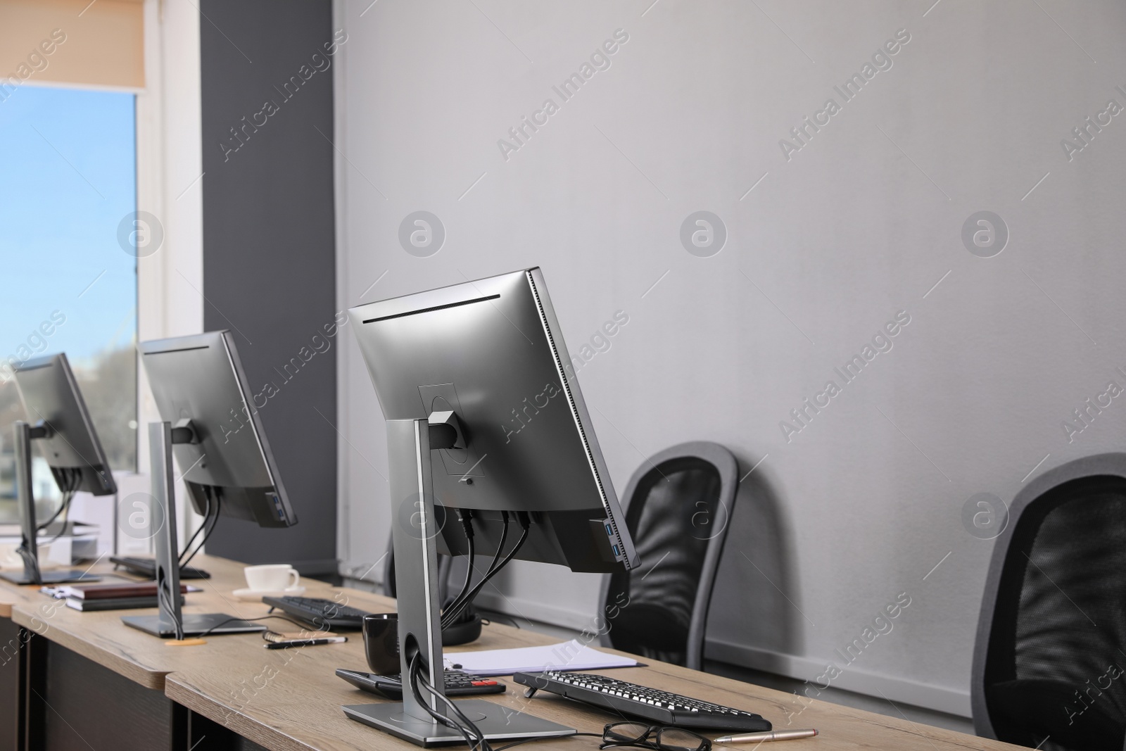 Photo of Open office interior. Modern workplaces with computers near light grey wall