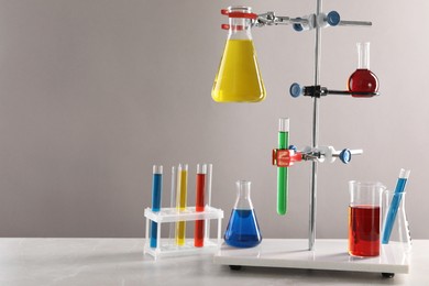 Retort stand and laboratory glassware with liquids on table against light grey background, space for text