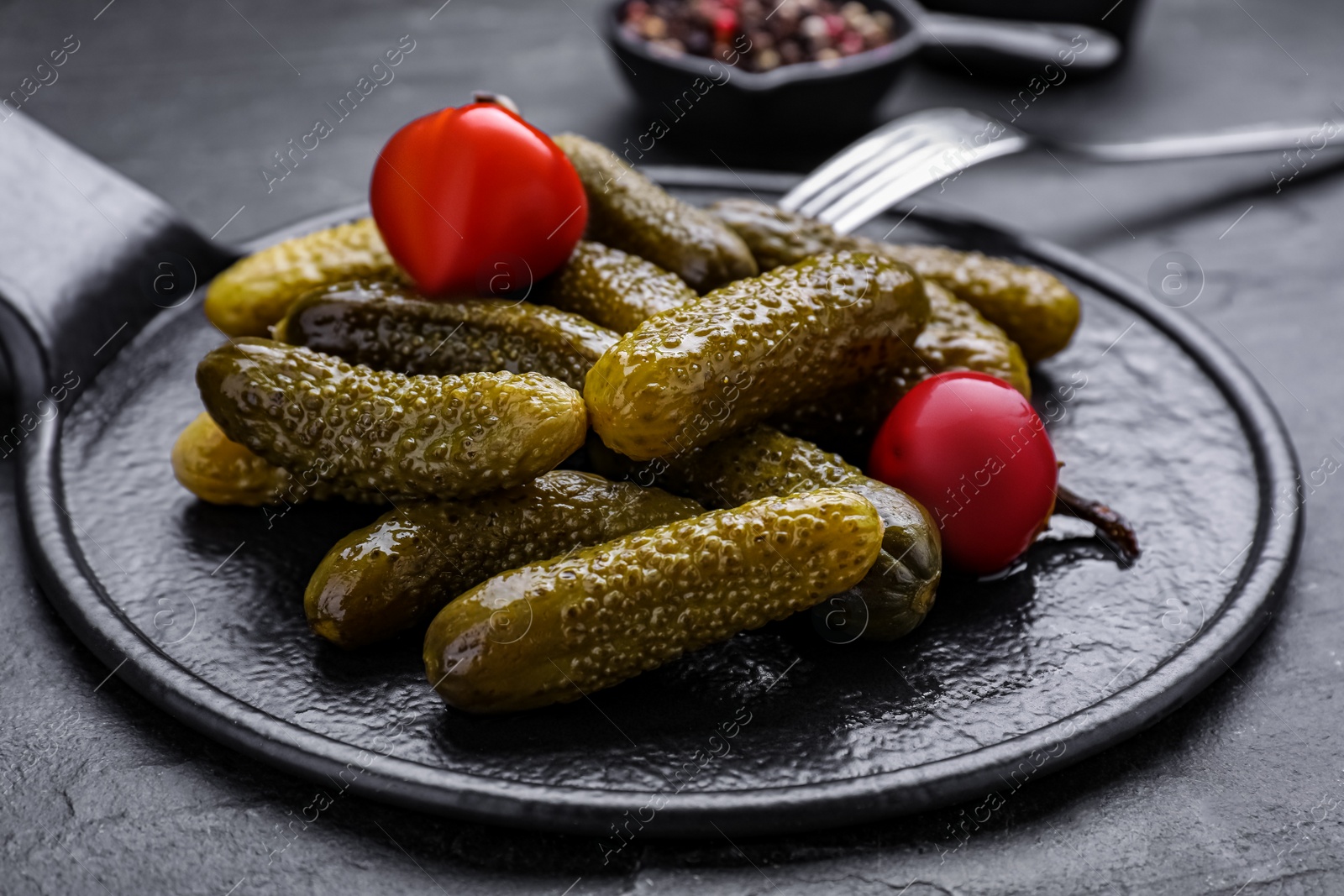 Photo of Serving board with pickled cucumbers and peppers on black table, closeup