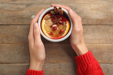 Young woman holding cup with tasty mulled wine at wooden table, top view