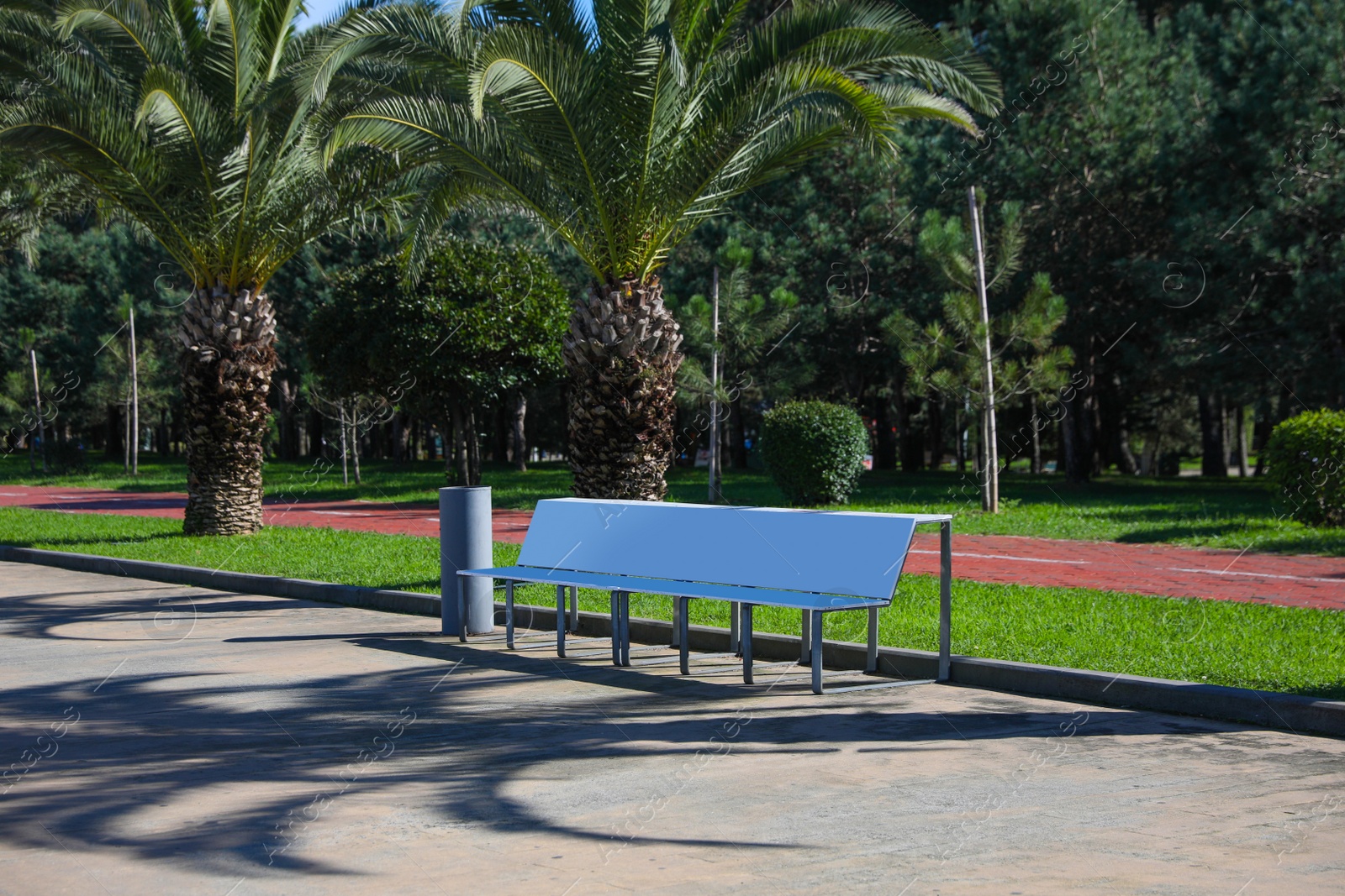 Photo of White metal bench and trash can in park